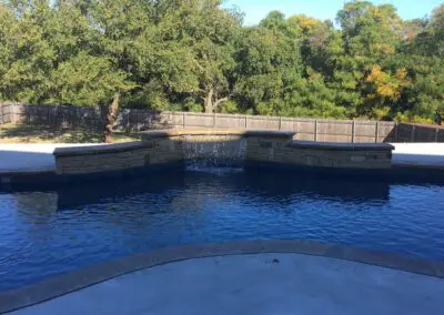 Backyard freeform blue swimming pool with stone spa and waterfall
