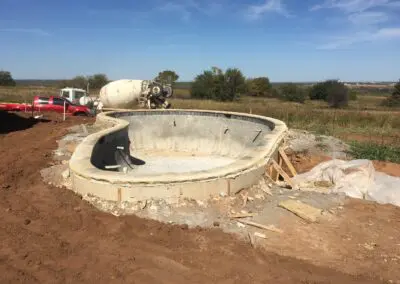 Concrete in-ground pool shell under construction on rural lot with trucks