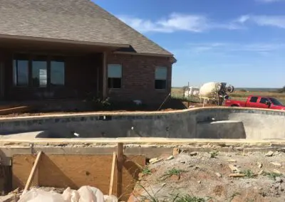 Residential backyard pool under construction in front of brick house with cement truck