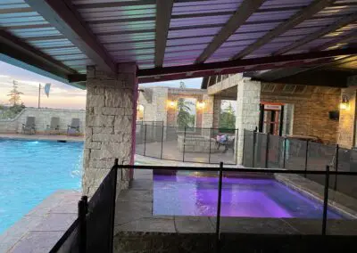 Covered backyard pool and illuminated purple spa with stone columns
