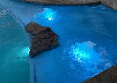 Pool spa with illuminated blue water, bubbling jets, and decorative rocks