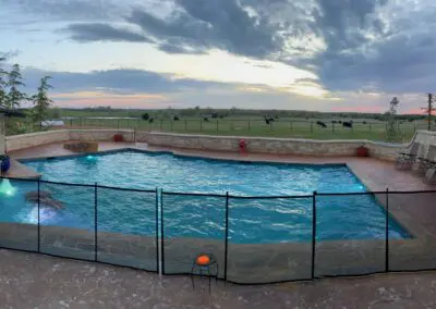 Backyard pool with spa, safety fence, stone patio, and sunset countryside