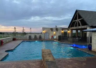 Backyard stone pool and pavilion at sunset with seating and blue lights