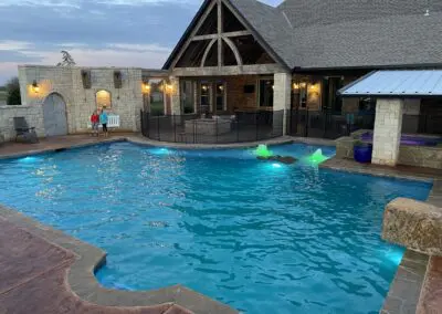 Residential backyard pool with illuminated fountains and stone patio