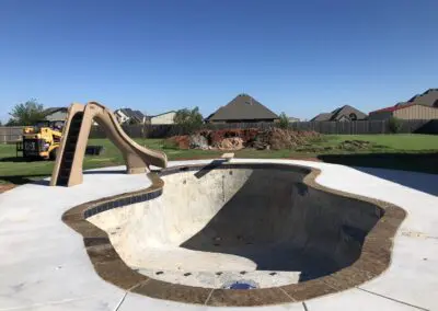 Empty inground pool under construction with slide and backyard equipment
