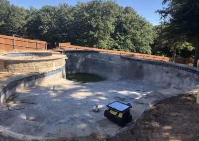 unfinished concrete backyard pool under construction with nearby spa and toolbag