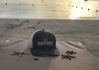 Trophy Pools trucker hat on beach towel with starfish at sunrise