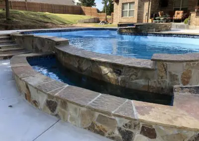 Backyard stone-trimmed pool with raised spa and cascading water