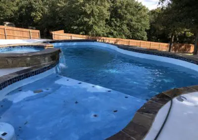 Swimming pool and raised spa with waterfall, blue plaster, backyard fence