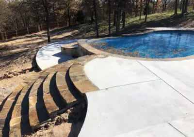 Pool with curved stone steps and concrete patio surrounded by trees