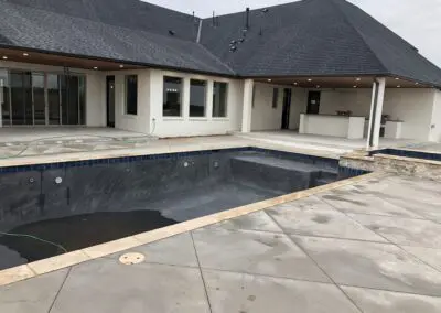 Backyard modern home with unfinished in-ground pool and wet concrete patio