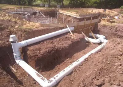 Swimming pool construction site with large white PVC drainage pipes and rebar