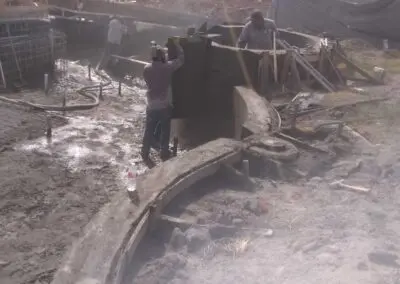 construction crew pouring and shaping concrete pool shell on muddy site