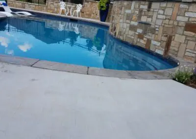 Backyard in-ground pool with stone retaining wall and white patio chairs