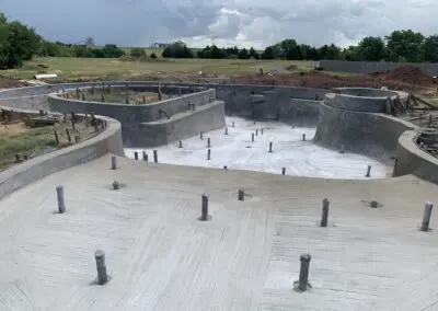Residential concrete pool shell under construction on grassy backyard with trees