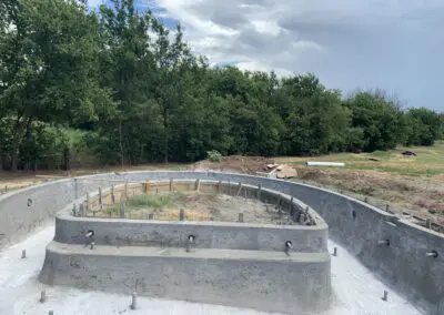 Residential concrete pool shell under construction on grassy backyard with trees