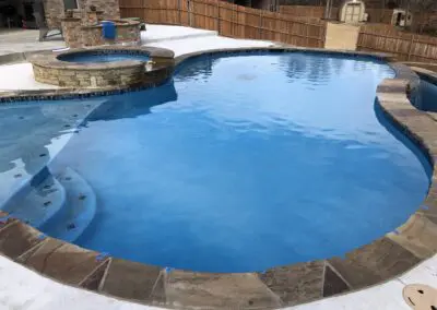 Residential curved inground pool and raised spa with stone coping and concrete deck