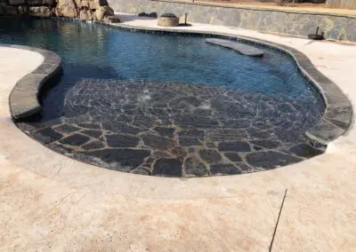 In-ground pool with shallow tanning ledge and stone coping