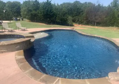 Backyard freeform blue pool with spa, loungers, and surrounding trees
