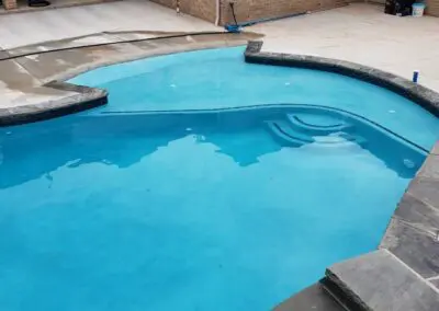 Newly finished backyard pool with spa, blue water, and stone coping