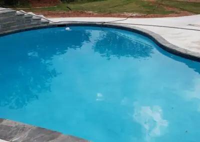 Residential blue in-ground swimming pool with stone coping and concrete deck