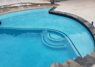Residential blue in-ground swimming pool with stone coping and concrete deck