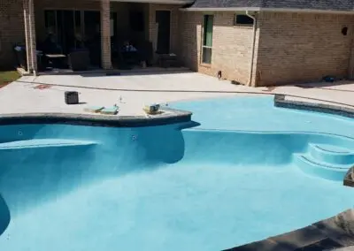 Residential blue in-ground swimming pool with stone coping and concrete deck