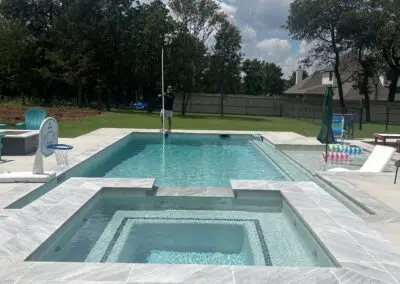 Modern backyard pool and raised spa with patio, lawn, and cloudy sky