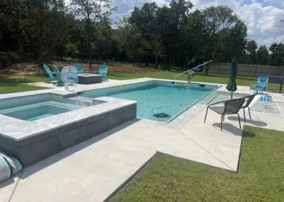 Backyard modern pool with spa, patio chairs, basketball hoop, technician cleaning