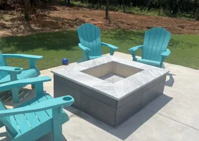 Outdoor concrete patio with square marble-topped fire pit and teal Adirondack chairs