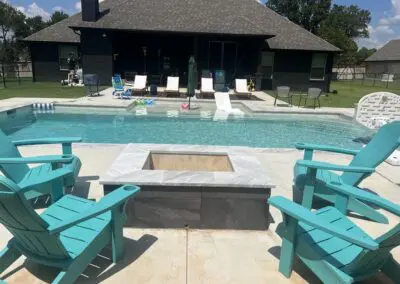 Backyard pool with slide, turquoise Adirondack chairs, and central firepit