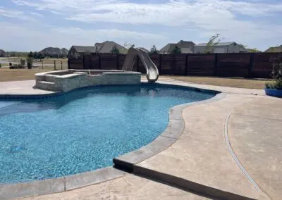 Backyard swimming pool with slide, spa, stamped concrete patio