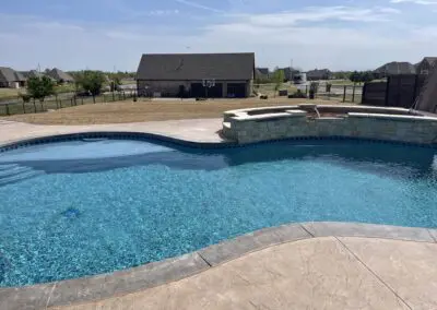 Backyard blue swimming pool with stone spa and concrete deck