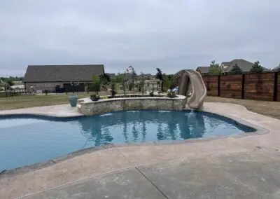 Backyard freeform pool with stone raised wall and tan slide