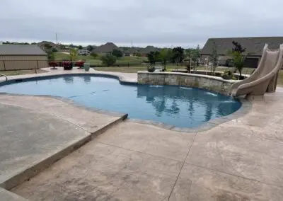 Backyard freeform pool with stone water feature and slide, concrete decking