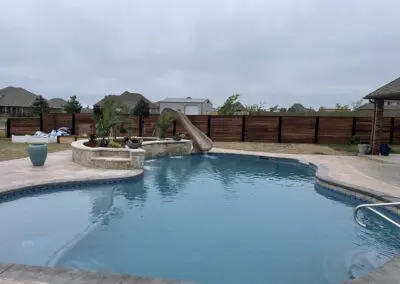 Backyard freeform pool with stone water feature and slide, concrete decking