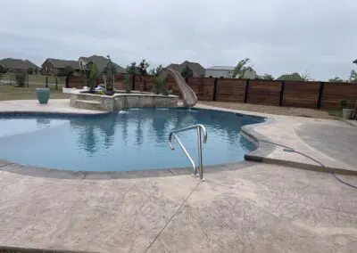 Backyard freeform pool with stone water feature and slide, concrete decking