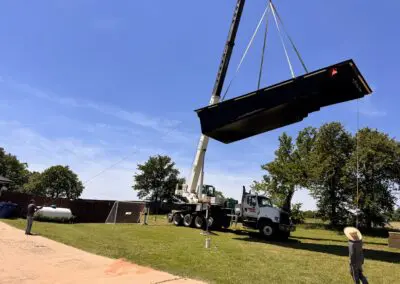 Crane lifting a fiberglass pool shell over backyard while workers guide it