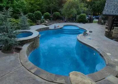 Residential freeform blue pool and attached spa at sunset, stone deck