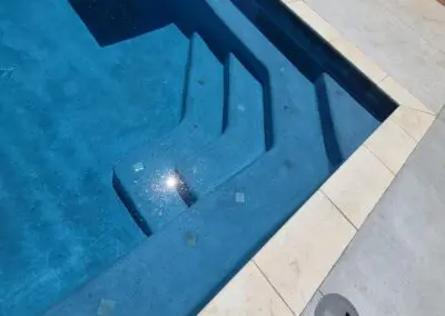 Person standing at tiled pool edge looking down at blue pool steps and sun reflection