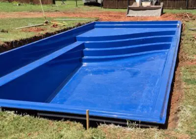 Blue fiberglass pool shell installed in backyard with construction equipment
