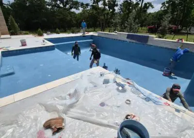 Workers applying blue finish inside a residential inground pool under construction