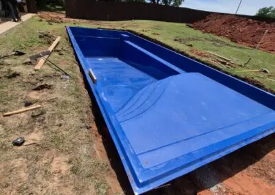 Blue fiberglass swim spa shell installed in backyard trench during pool construction