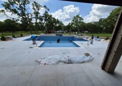Workers finishing blue-tiled backyard pool installation on concrete patio