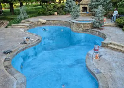Empty backyard swimming pool with blue plaster, stone deck, spa, and fireplace