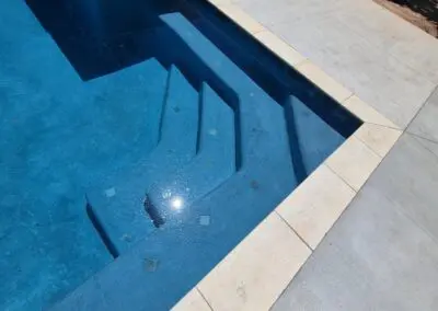 Person standing at pool edge overlooking blue pool steps and raised spa