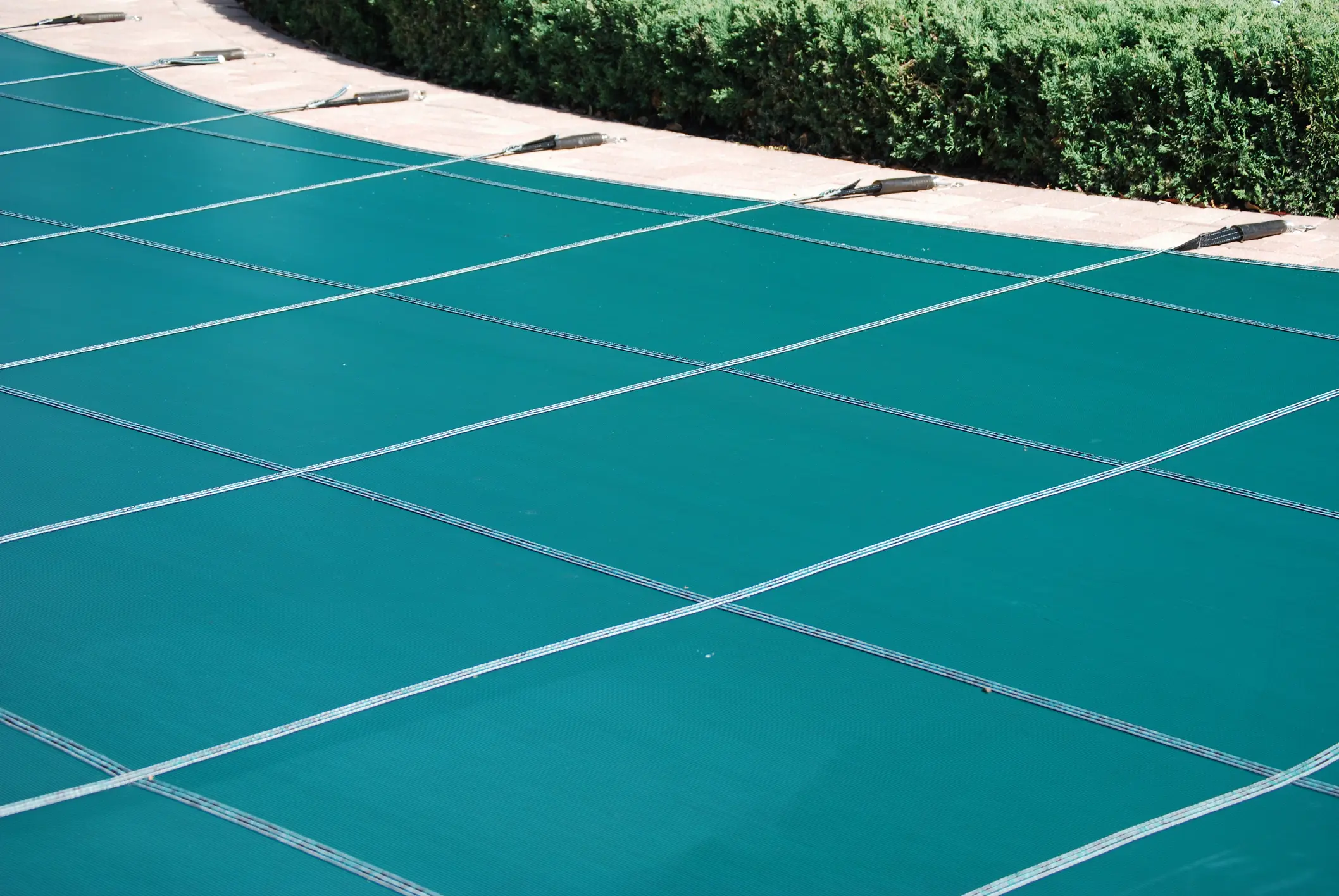 teal safety pool cover secured with straps over residential pool