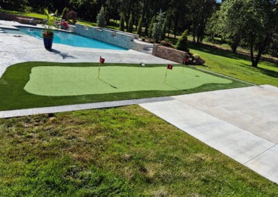 Backyard artificial putting green with three numbered flags beside a pool