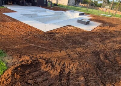 new concrete pool shell with surrounding excavated yard and nearby house