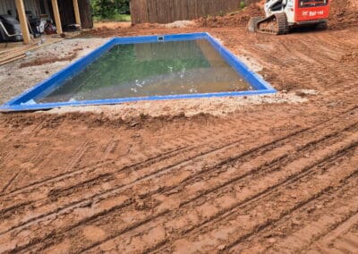 Residential backyard pool shell installation with track loader and muddy yard